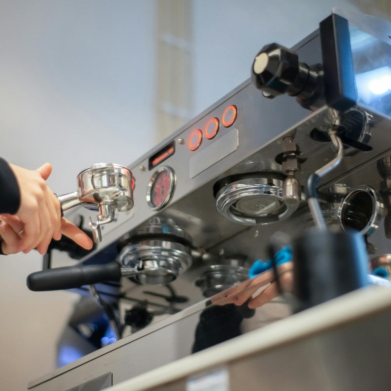 upward facing photo of a traditional coffee machine on a counter top with a barista preparing coffee